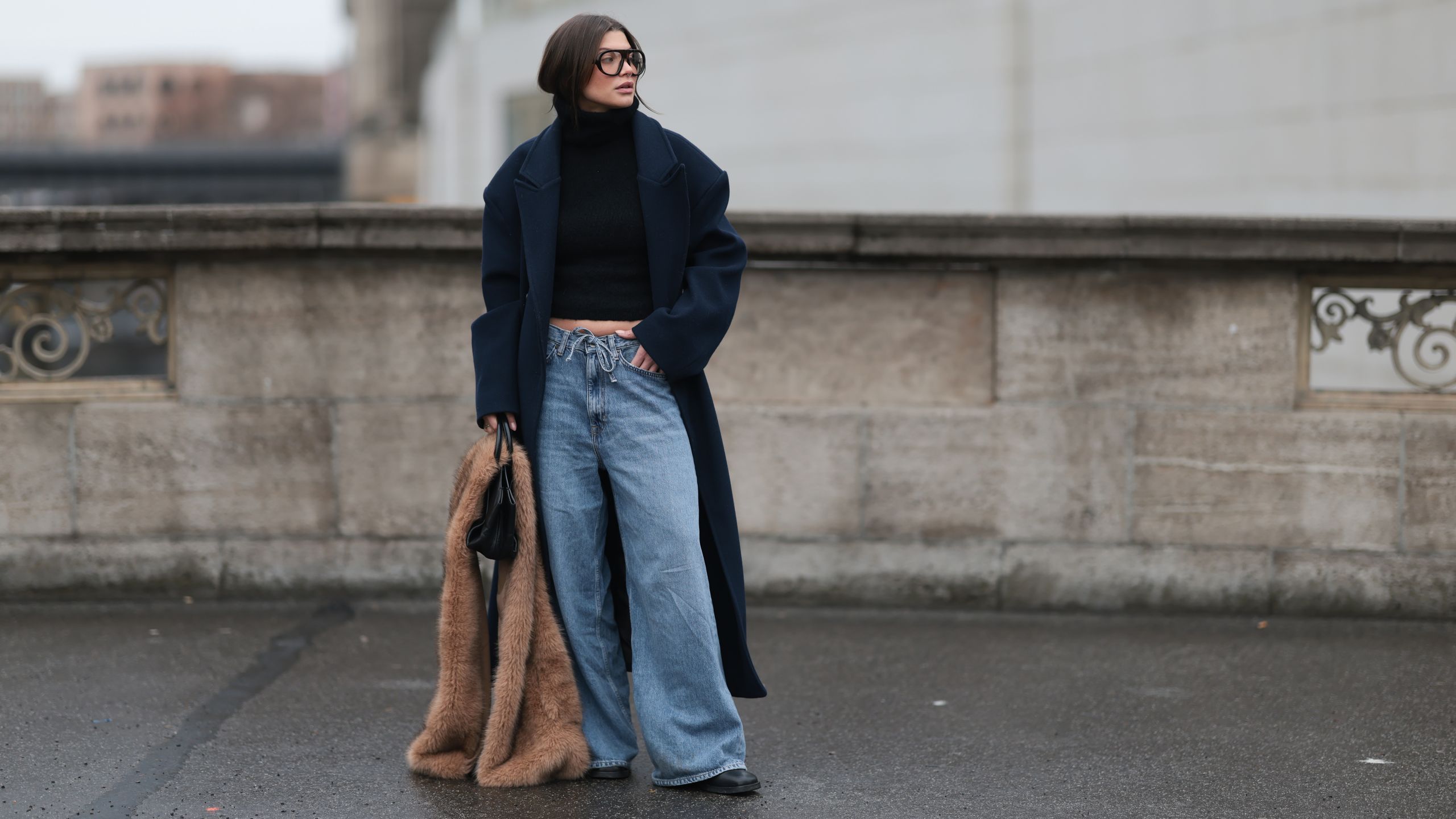 mujer con vaqueros wide leg claros jersey negro abrigo largo y estola de pelo marrón