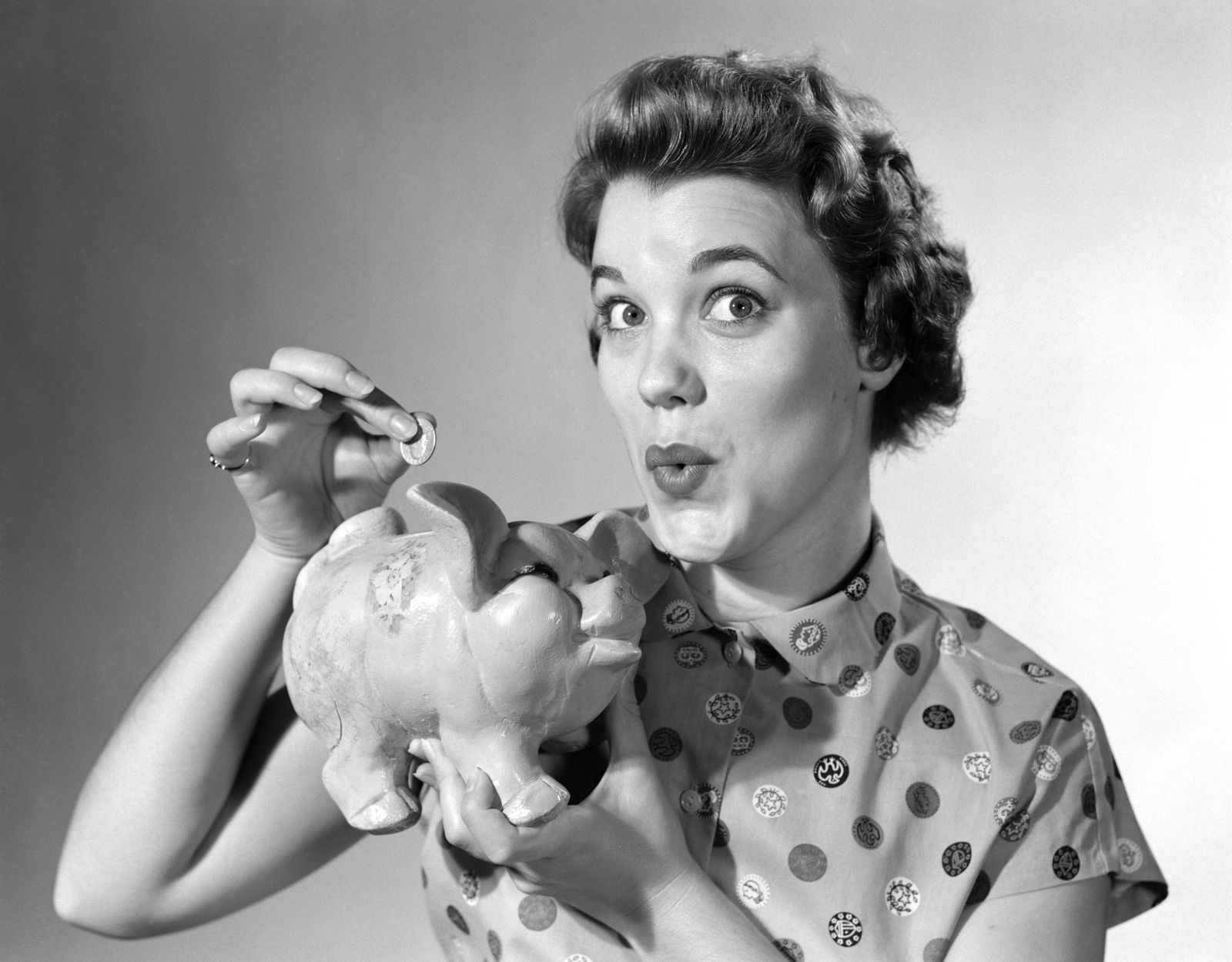 1950s WOMAN LOOKING AT CAMERA DROPPING MONEY IN PIGGY BANK